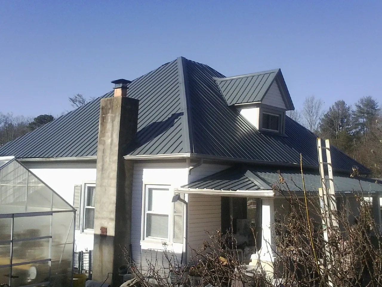 Dark blue standing seam metal roof on a white farmhouse with dormer — Slate & Tile Roof Repair by Roofing Brothers in Bullock