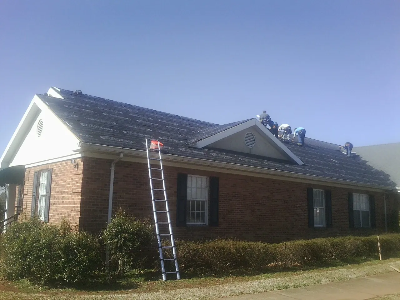 Crew tearing shingles off a brick ranch roof with a ladder set — Emergency Roof Repair work by our crew in Bullock