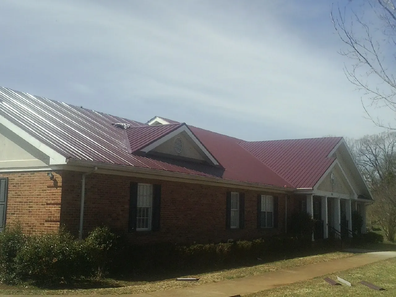 Red metal roof with gabled entries on a long brick building, from a Hail Damage Roof Repair job in Bullock