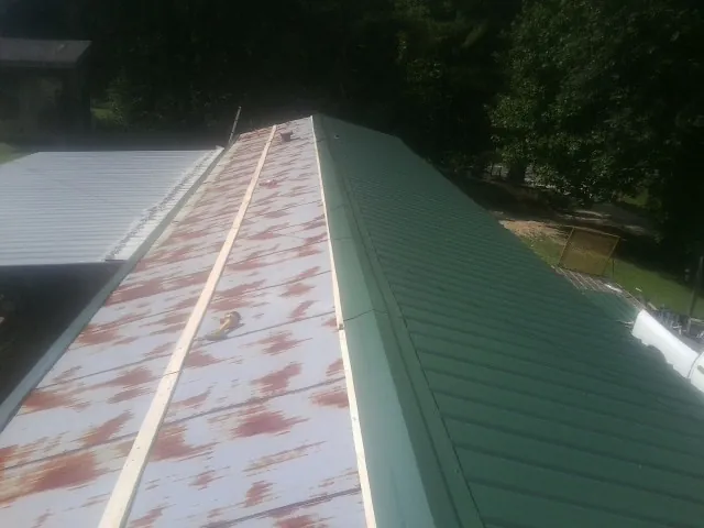 Old rusted panels beside newly installed green metal roofing — Wind Damage Roof Repair by Roofing Brothers in Bullock