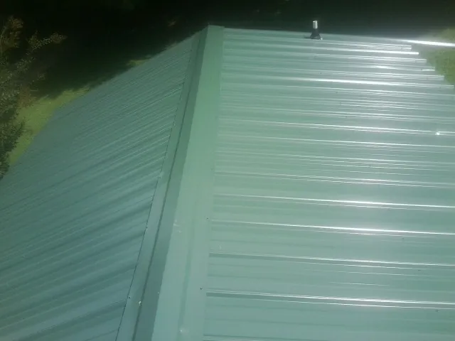 New green metal panels meeting at the ridge of a roof — Flat Roof Repair work by our crew in Bullock