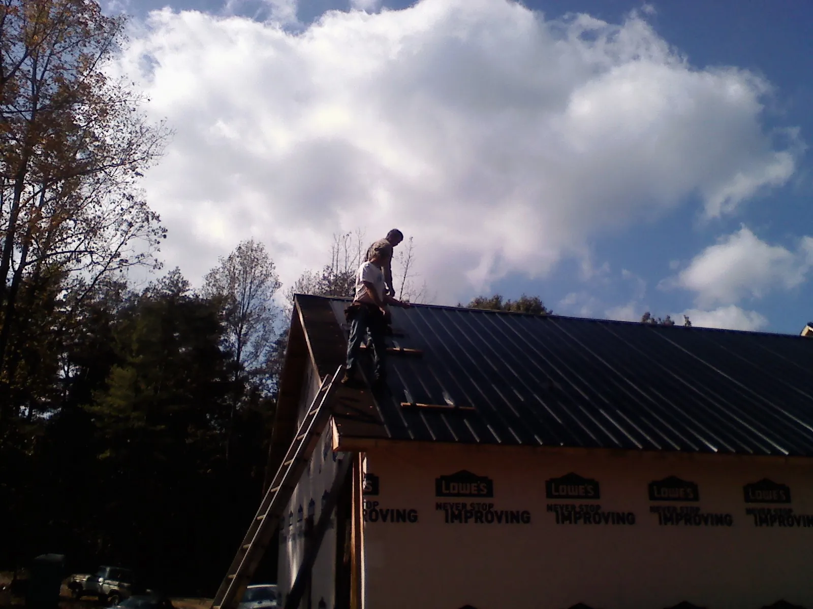 Roofer fastening dark metal panels high against a cloudy sky, from a Roof Inspection job in Bullock