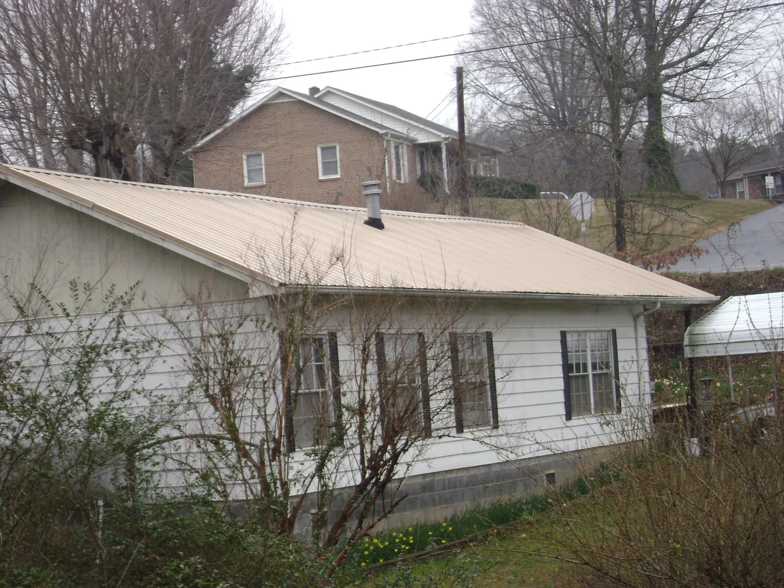 Tan metal roof on a white sided house set into a hillside — Commercial Roofing by Roofing Brothers in Bullock
