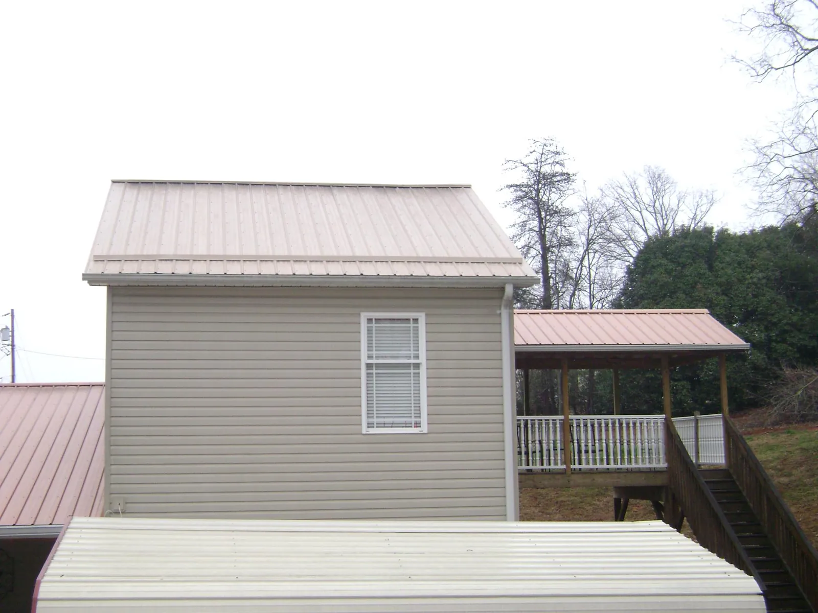 Tan metal roofs on a two story addition and attached porch, from a Roof Replacement job in Bullock